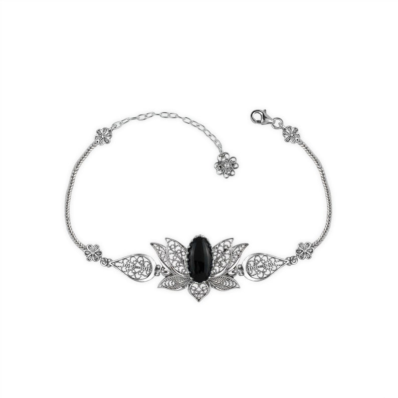 May include: A silver bracelet with a black gemstone set in a filigree lotus flower design.