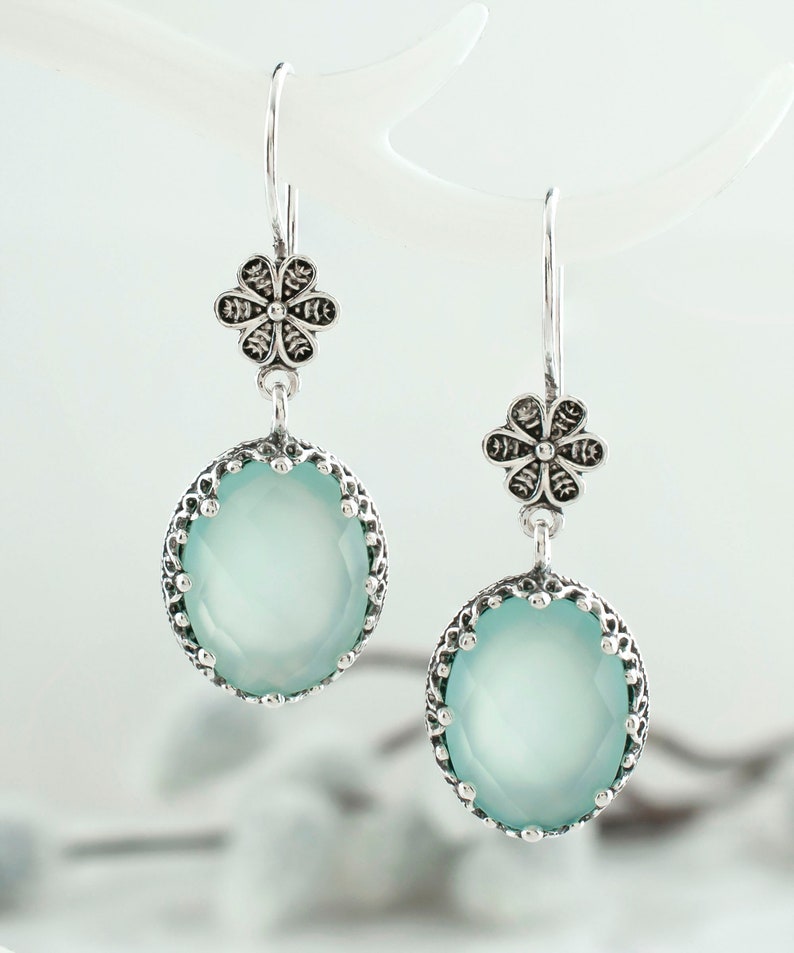 May include: Silver dangle earrings with a light blue gemstone and a silver flower charm.