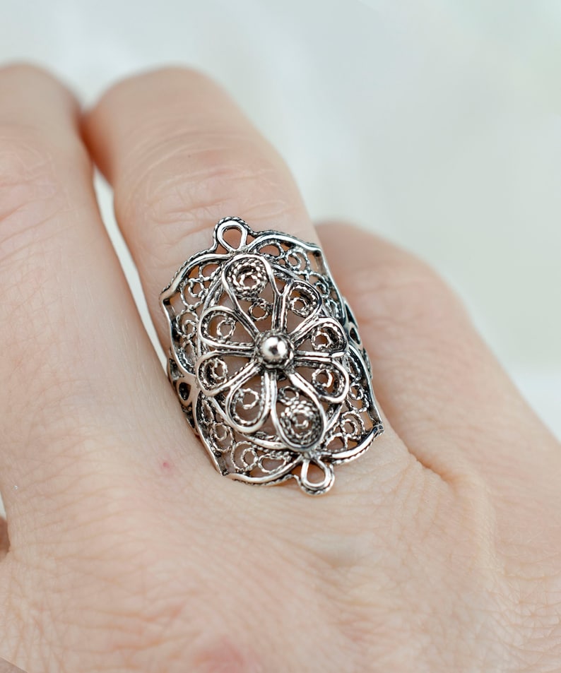 May include: A silver filigree ring with a floral design. The ring is wide and has a delicate, intricate pattern.