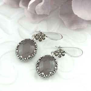 May include: A pair of silver earrings with a gray oval stone and a floral design. The earrings have a delicate, feminine look.