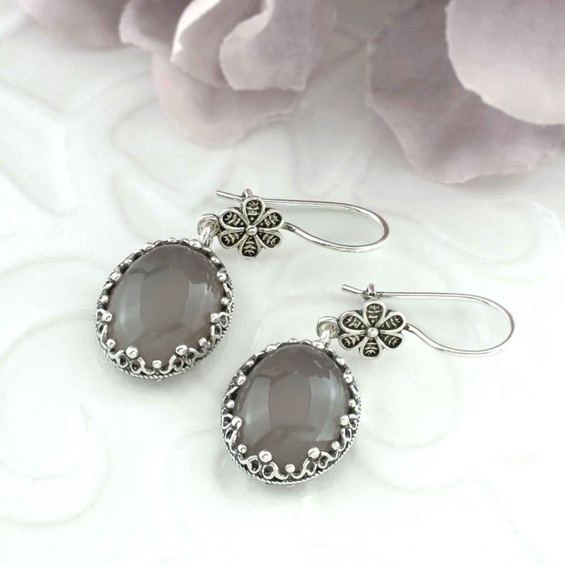 May include: A pair of silver earrings with a gray oval stone and a floral design. The earrings have a delicate, feminine look.