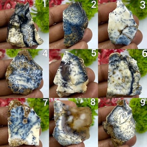 May include: A collection of nine numbered dendritic opal specimens, each featuring unique branching, fern-like black or dark blue inclusions set against a creamy white, translucent, or tan base, displayed as individual rough-cut stone pieces.