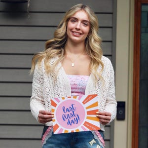 Teen girl holding a Last First Day sign or photo prop for the class of 2026, sunrise design in pink and orange