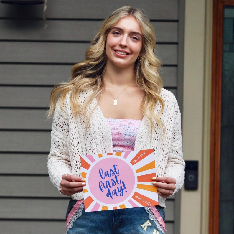 Teen girl holding a Last First Day sign or photo prop for the class of 2026, sunrise design in pink and orange