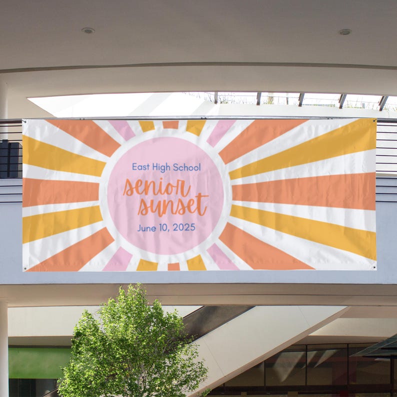 Op de afbeelding: Een rechthoekige banner met een zonnestraalpatroon in tinten oranje, geel en roze. Een centrale roze cirkel bevat de blauwe tekst East High School, de oranje cursieve tekst senior sunset en de blauwe datum 10 juni 2025.
