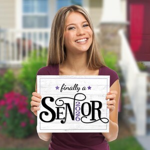 Teen girl standing outside in front of a house holding a Purple first day of senior year sign for the class of 2026