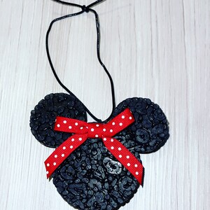 May include: Black car air freshener shaped like Mickey Mouse with a red bow with white polka dots. The air freshener is hanging from a black string.