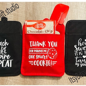 May include: Three black oven mitts with white text. The left mitt says "teach bake inspire repeat". The middle mitt is red and says "Thank you for making me one smart cookie!" with a chocolate chip cookie graphic. The right mitt says "how sweet it is to be taught by you" with a pencil and hearts.