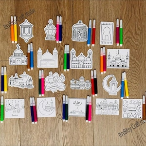 May include: A collection of Ramadan-themed coloring pages and markers. The pages feature mosque and lantern designs, along with the text "Ramadan Mubarak" and "Ramadan". The markers are in various colors, including yellow, orange, green, blue, pink, and black.