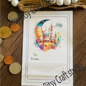 May include: A white card with a colorful illustration of a mosque and crescent moon. The card has a clear plastic insert for a gift card or money. The text on the card reads "Eid al-Fitr".