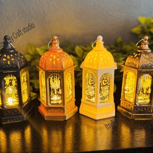 May include: Four decorative lanterns in varying colors, including black, orange, and gold, are arranged on a dark surface. Each lantern has intricate cut-out designs and emits a warm, inviting glow. The lanterns are likely for home decor.
