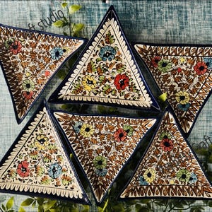 Może przedstawiać: Sześć trójkątnych ceramicznych talerzy z kwiatowym wzorem. Talerze mają białą podstawę z brązowymi i kolorowymi wzorami kwiatowymi, ciemnoniebieską obwódkę i dekoracyjną krawędź. Talerze są ułożone na niebieskiej powierzchni.