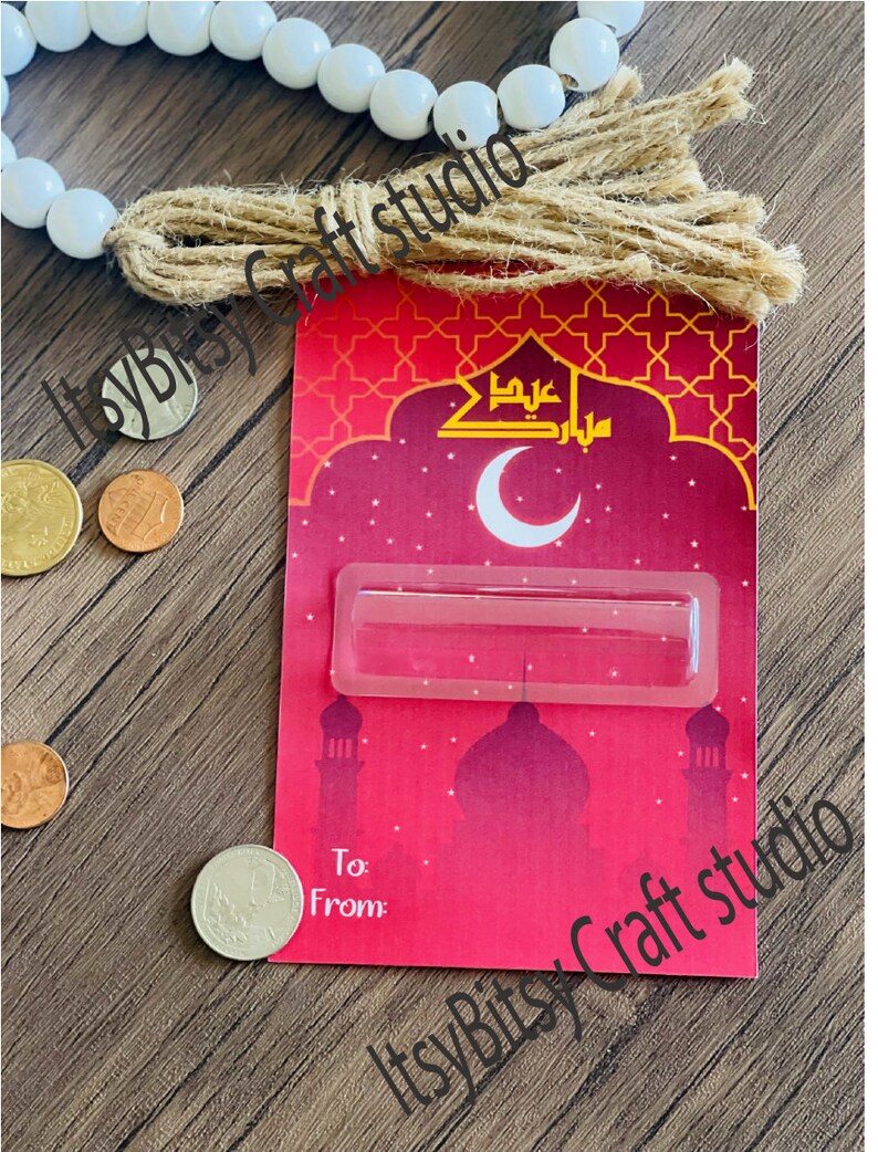 May include: Red and gold card with a crescent moon and Arabic text. The card has a clear plastic window for a gift card or money. The card says "To" and "From".