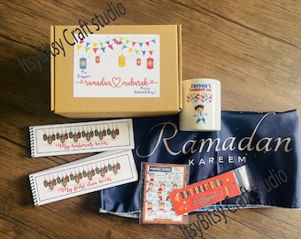 May include: A Ramadan gift box set with a blue fabric bag, a mug with a boy's illustration and the text "Zayyan's Sadaqah Jar", two small books with the text "My Kalimas Book" and "My First Dua Book", a red and yellow beaded keychain with the text "Don't Forget to Say Alhamdulillah", and a card with the text "Making Husul" and illustrations of people.