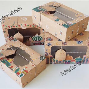 May include: Four stacked, brown cardboard boxes with clear window panels. The boxes are decorated with colorful illustrations of mosques, crescent moons, and stars. The text "ItsyBitsy Craft studio" is printed on the boxes.