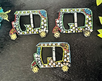 May include: Three colourful, mosaic-style, decorative, auto rickshaw ornaments. Each rickshaw is a different colour and has a black and white chequered pattern. The ornaments are made of glass and have a shiny finish.