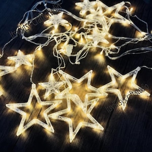 May include: A string of white fairy lights with star-shaped bulbs. The lights are strung together with clear wire and are lit up, casting a warm glow.