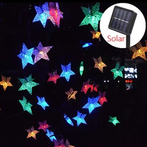 May include: A string of solar-powered fairy lights with star-shaped bulbs in various colors, including red, blue, green, and purple. The lights are strung together with a clear wire and have a solar panel with the word "Solar" printed on it.
