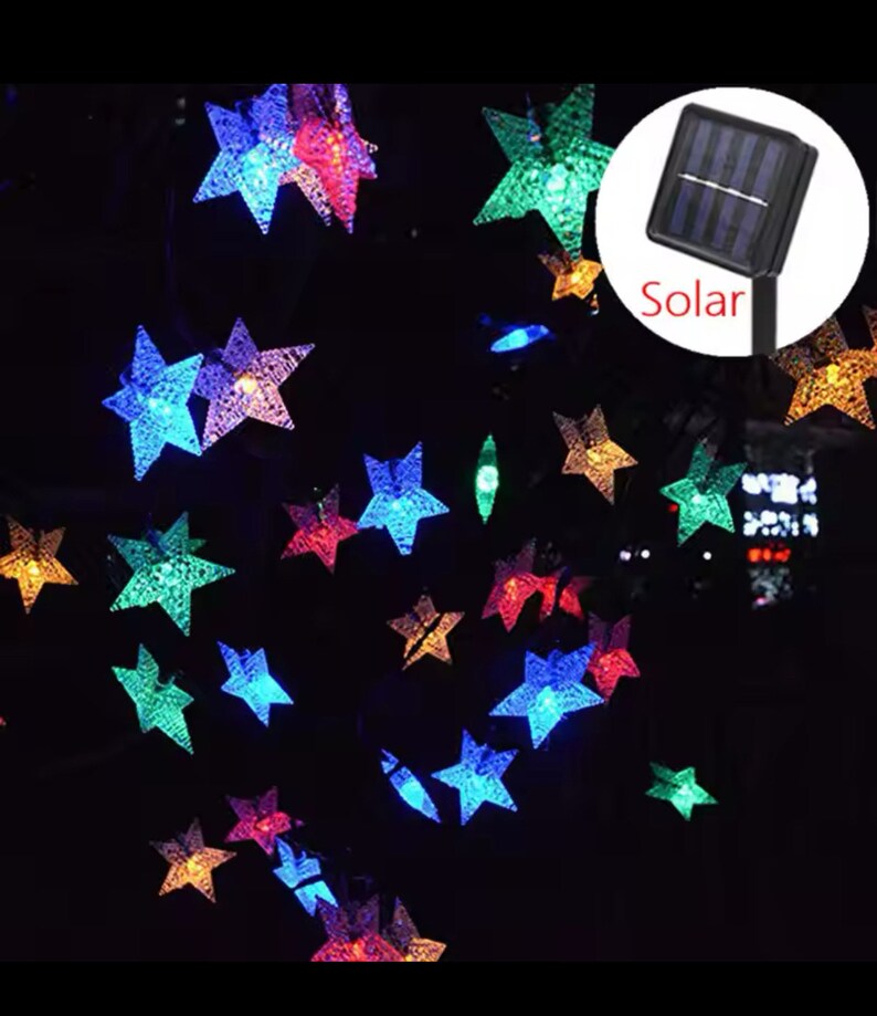 May include: A string of solar-powered fairy lights with star-shaped bulbs in various colors, including red, blue, green, and purple. The lights are strung together with a clear wire and have a solar panel with the word "Solar" printed on it.