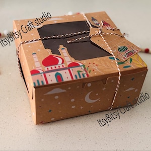May include: A brown cardboard gift box with a clear window, tied with twine. The box is decorated with a mosque design in red, pink, and teal. The text "ItsyBitsy Craft studio" is printed on the box.
