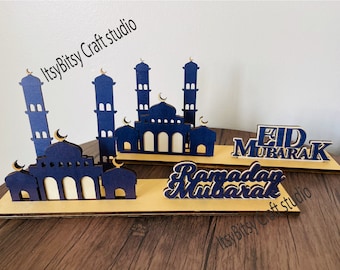 May include: Three wooden decorations with blue and white paint. The decorations feature a mosque design and the words "Eid Mubarak" and "Ramadan Mubarak".