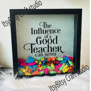 Könnte beinhalten: Eine schwarze Schattenbox mit silbernem Glitzerhintergrund und dem Text "The Influence of a Good Teacher can never be Erased". Die Box ist mit bunten Bleistifträdern gefüllt.
