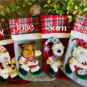 Könnte beinhalten: Vier rote und weiße karierte Weihnachtsstrümpfe mit verschiedenen Figuren. Die Strümpfe sind mit den Namen Alex, Jose, Sam und Jessica personalisiert.