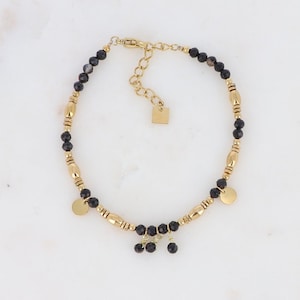 Peut inclure: Bracelet en or avec des perles noires et des breloques dorées. Le bracelet a une petite étiquette dorée avec le mot "Love" dessus.