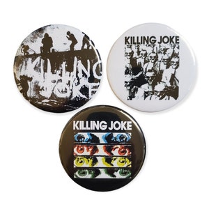May include: Three round button pins with the band name "Killing Joke" printed on each. The first pin features a black and white image of a band on stage. The second pin features a black and white image of a crowd of people. The third pin features a black background with a colorful image of multiple eyes.