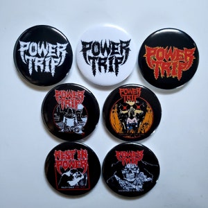 May include: A collection of seven round buttons with the band name "POWER TRIP" in a stylized font. The buttons feature black, white, and red backgrounds with various graphics, including a skull, a figure, and the text "REST IN POWER".
