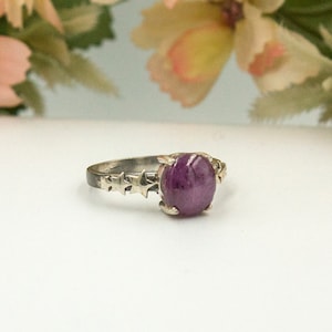May include: A silver ring featuring a purple gemstone and star-shaped accents.