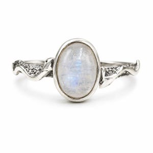 Op de afbeelding: Een zilveren ring met een ovale maansteen cabochon in een gladde zetting. De ringband is vormgegeven met een gestructureerd, kronkelend slangontwerp dat om de vinger wikkelt, met gedetailleerde schubben en een gepolijste metalen afwerking.