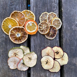 Puede incluir: Rebanadas de fruta seca dispuestas sobre una superficie de madera. Las rebanadas incluyen naranja, limón y manzana. La fruta está dispuesta en cuatro grupos, cada grupo contiene un tipo de fruta diferente.