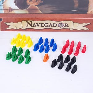 Puede incluir: Una colección de piezas de juego coloridas con forma de barcos. Las piezas son de varios colores, incluyendo amarillo, verde, azul, naranja, rojo y negro. La caja del juego dice "Navegador".