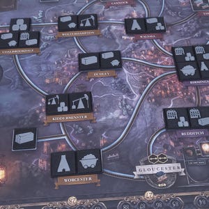 以下が含まれることがあります： 様々な都市名とトークンが書かれたゲームボード。トークンは白のシンボルが描かれた黒で、電車、クレーン、木材の山などがあります。ボードは濃いグレーで、薄いグレーの縁取りがされています。