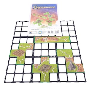 Könnte beinhalten: Ein Brettspiel-Set mit dem Titel "Carcassonne" auf der Box. Das Spiel enthält ein schwarzes Raster, grün umrandete Kacheln mit Landschaften und ein Spielbrett. Die Kacheln zeigen Straßen, Städte und Felder. Das Spiel ist für mehrere Spieler konzipiert.