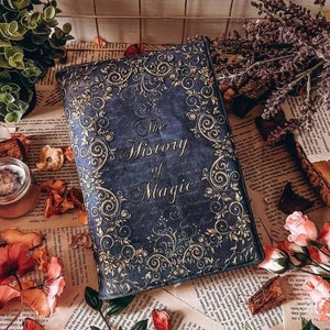 May include: A blue book with gold accents and the title "The History of Magic" on the cover. The book is surrounded by flowers and greenery.