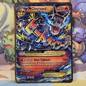 May include: A holographic Pokemon card featuring a blue and black Mega Charizard EX with a gold border. The card has a gold background with a black and white illustration of a Charizard. The card text reads "Mega Evolution rule" and "Heat Typhoon 100+".
