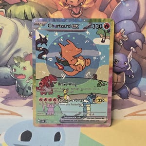 May include: A Charizard ex trading card featuring a whimsical, hand-drawn style illustration of a small orange dragon character floating in a blue circle. The card displays 330 HP, the attacks Brave Wing and Explosive Vortex, and various small colorful creature illustrations across the bottom and sides.