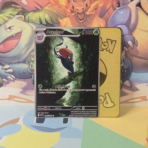 May include: A Pokémon trading card featuring Accelgor, with a red and black creature illustration set against a forest backdrop. The card has the text "Accelgor" and "Acid Spray". A gold-colored card is visible behind it.
