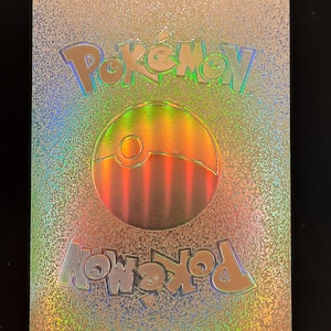 May include: A holographic Pokemon card back with a silver background and a rainbow colored Pokeball logo. The text "Pokemon" is printed in a silver font at the top and bottom of the card.