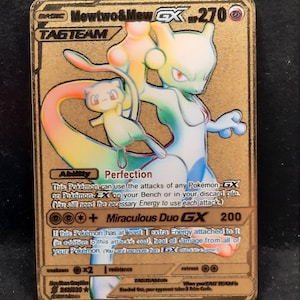 May include: A gold-colored Pokémon trading card featuring Mewtwo & Mew GX. The card has a holographic design with the text "TAG TEAM" and "Miraculous Duo GX 200". The card has a gold border and a black background.