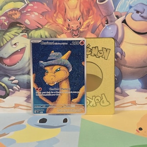 May include: A Pokémon trading card featuring Charizard wearing a hat, with the text "Charizard with Grey Hat" and "Charizard-Portrait". The card is set against a background of other Pokémon characters and a gold-colored card.