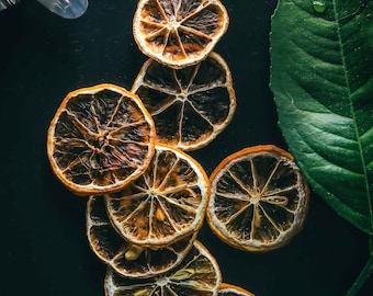 May include: Dried orange slices arranged in a circular pattern on a black background. The slices are a deep orange color and have a slightly translucent appearance.