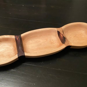 Könnte beinhalten: Ein Holztablett mit drei separaten Schalen. Das Tablett ist aus hellem Holz mit einem dunklen Holz-Akzentstreifen.