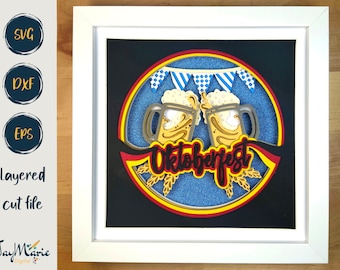 Puede incluir: Un diseño de papel artesanal en capas que presenta dos jarras de cerveza con espuma en la parte superior, una pancarta con banderas a cuadros azules y blancas, y la palabra "Oktoberfest" en letras rojas y negras. El diseño está sobre un fondo azul con un borde amarillo, rojo y negro.