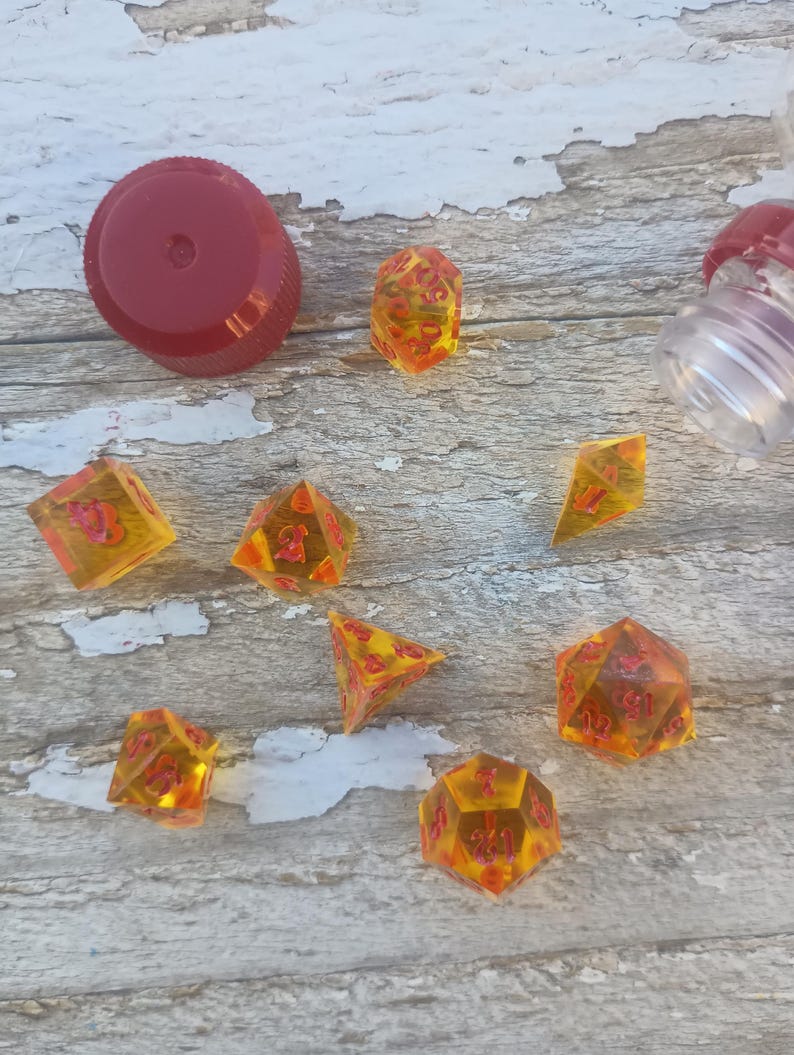 Puede incluir: Un conjunto de ocho dados de &aacute;mbar transl&uacute;cidos con n&uacute;meros rojos. Los dados est&aacute;n esparcidos sobre una superficie de madera clara.