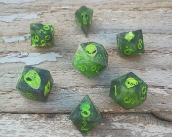 May include: Set of seven green and black dice with alien faces and numbers. The dice are made of clear resin with green and black swirls.