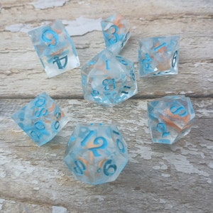 May include: Set of seven blue and white dice with gold flecks. The dice are numbered 1 through 6 and 12. The dice are on a wooden surface.