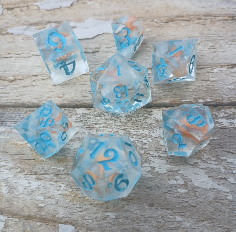 May include: Set of seven blue and white dice with gold flecks. The dice are numbered 1 through 6 and 12. The dice are on a wooden surface.